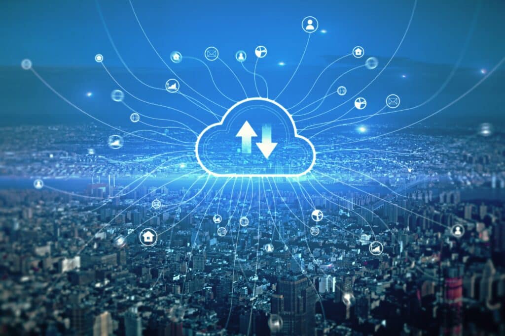 Imagem de uma cidade vista do alto, com um ícone holográfico de nuvem ao centro e setas de upload e download, conectado a diversos símbolos digitais por linhas luminosas, representando computação em nuvem, armazenamento de dados e conectividade urbana.