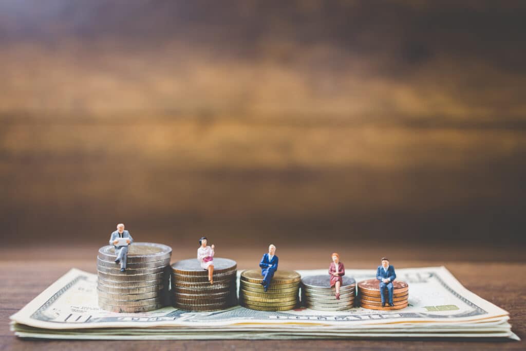 Miniaturas de pessoas sobre pilhas de moedas representando o Customer Lifetime Value e o aumento do valor de cada cliente para empresas SaaS.
