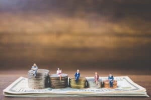Miniaturas de pessoas sobre pilhas de moedas representando o Customer Lifetime Value e o aumento do valor de cada cliente para empresas SaaS.