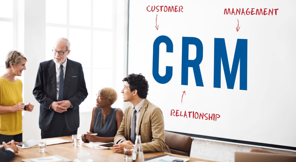 Profissionais em reunião corporativa diante de uma tela com a sigla CRM, representando gestão de relacionamento com clientes.
