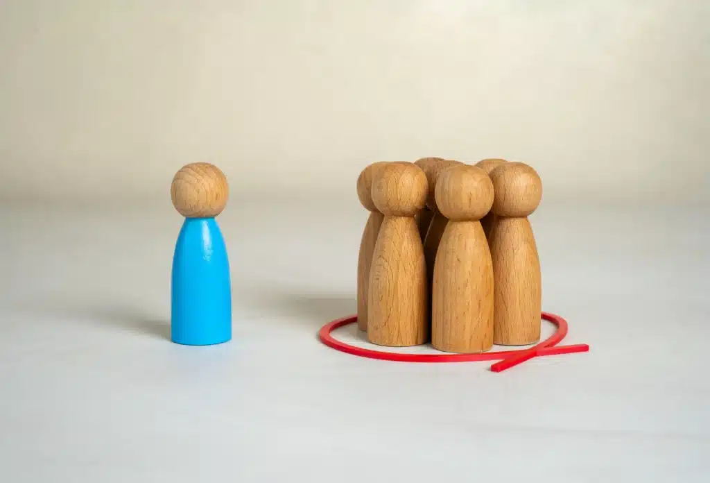 Figura de madeira azul separada de um grupo de figuras de madeira cercadas por um círculo vermelho, representando exclusão, diferenciação e pertencimento.